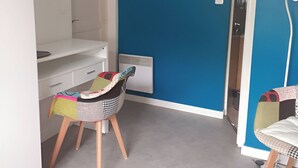 A small, bright room with a blue accent wall, a white desk, two chairs, and a radiator. - Quiet T1 in St Marc sur Mer, 5 min walk to the beach, terrace and large bed! (Saint-Nazaire)