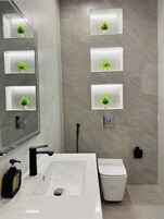 Un baño moderno con un espejo grande, un lavamanos blanco y un inodoro. Hay cuatro espejos cuadrados en la pared, cada uno con una pequeña planta.