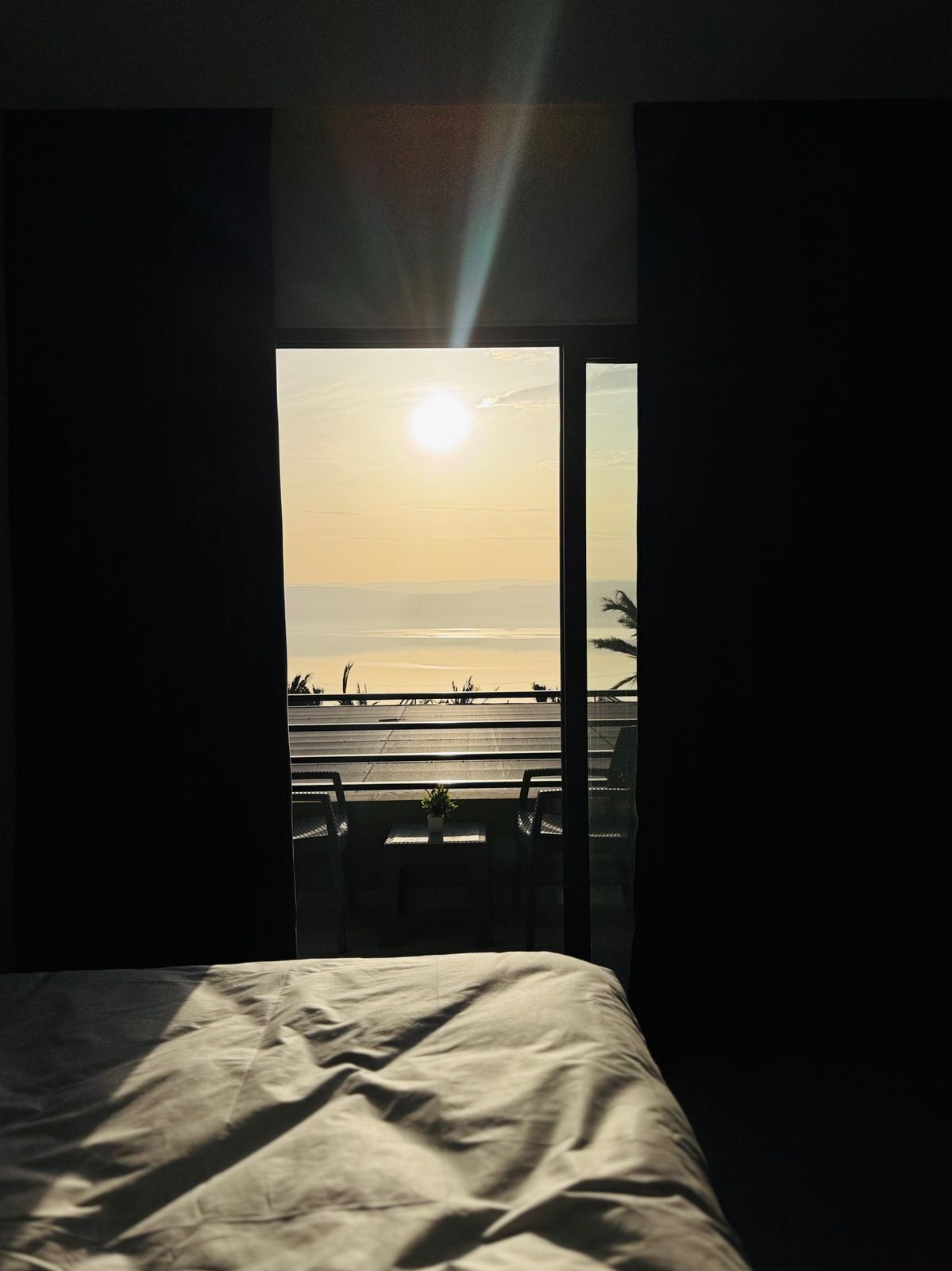 A room with a bed, a view of the beach, and a balcony with chairs and a table.