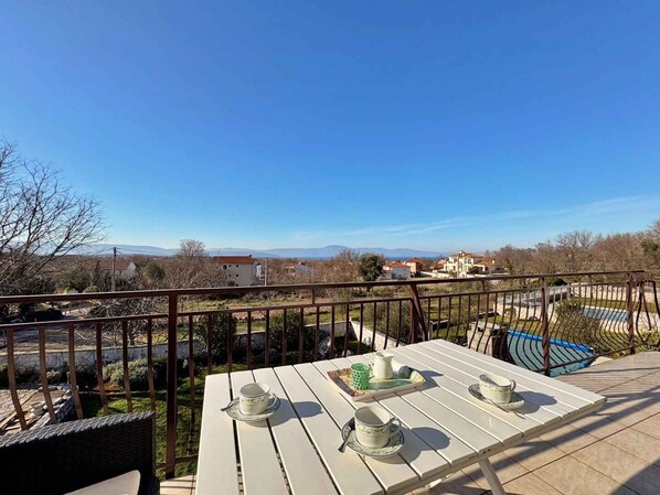 A terrace with a table set for tea, overlooking a scenic landscape with buildings and mountains.