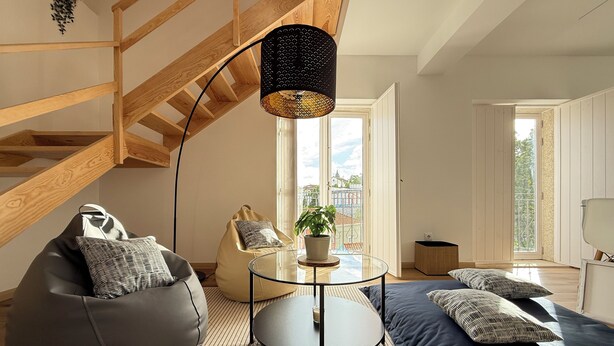 Ett modernt vardagsrum med högt tak, ett soffbord i glas, en sittpuff, en soffa och en krukväxt.