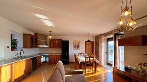 Cozinha ampla com armários de madeira, espaço de jantar com mesa e cadeiras, e um sofá.