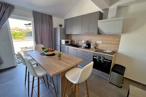 Una cocina moderna con armarios grises, encimera de madera y una zona de comedor con sillas blancas.