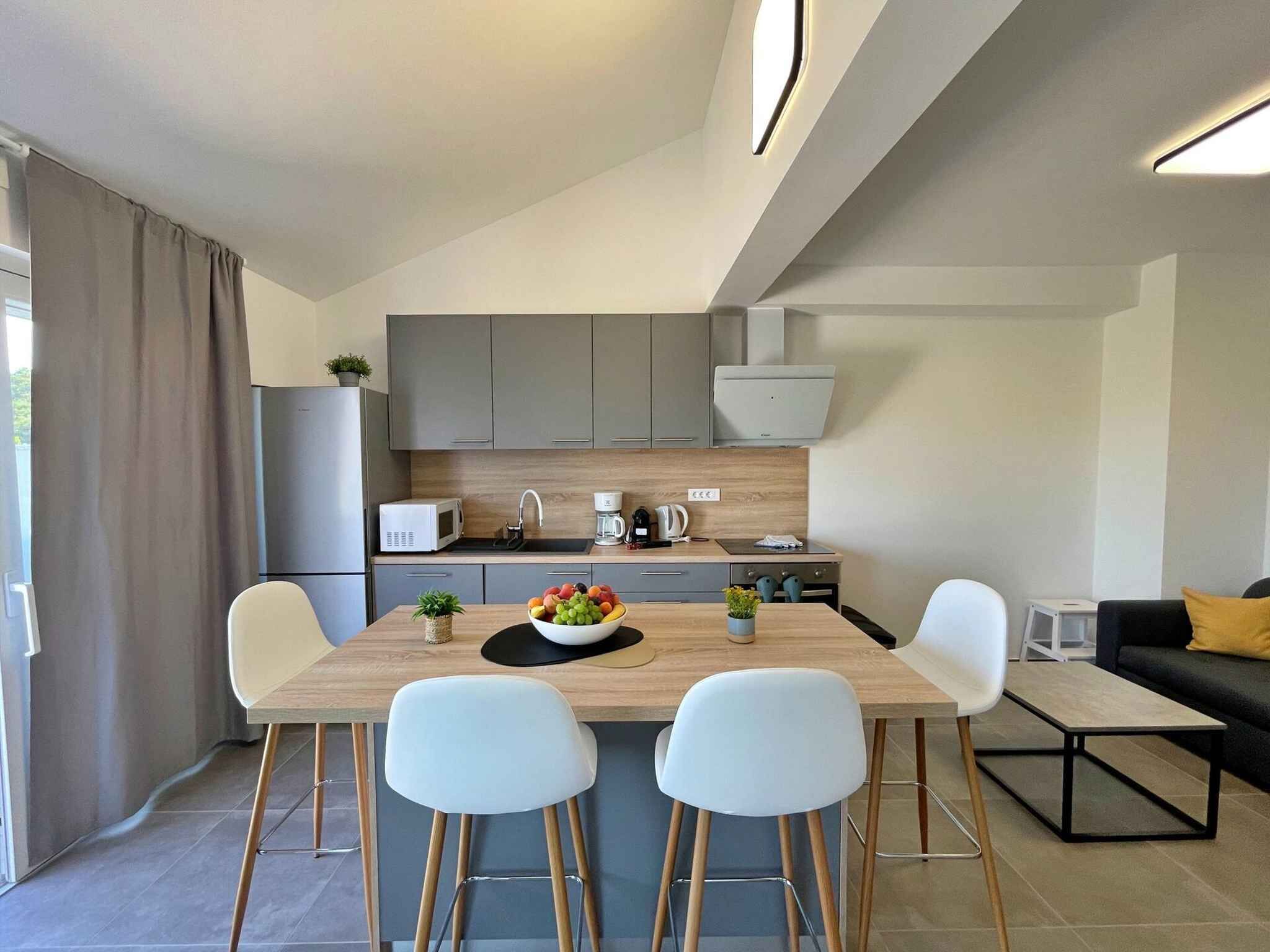 A modern kitchen with grey cabinets, a wooden countertop, and a dining area with two white chairs and a table.