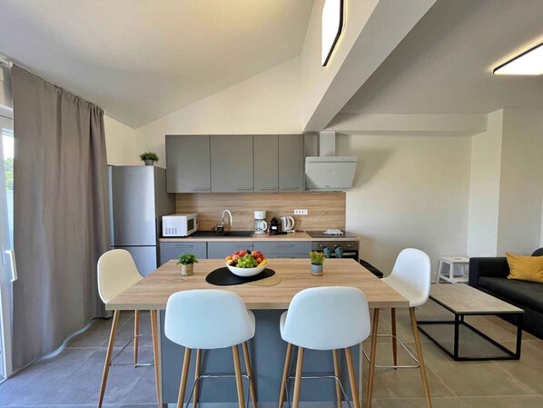 A modern kitchen with grey cabinets, a wooden countertop, and a dining area with two white chairs and a table.