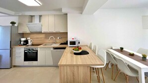 A modern kitchen with a central island, white cabinets, and a dining area with a long table and chairs. - Holiday apartment, modernly furnished, with air conditioning (Šilo)