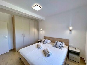 Quarto de hotel moderno com uma cama grande, duas mesas de cabeceira, um guarda-roupa e uma luminária no teto.