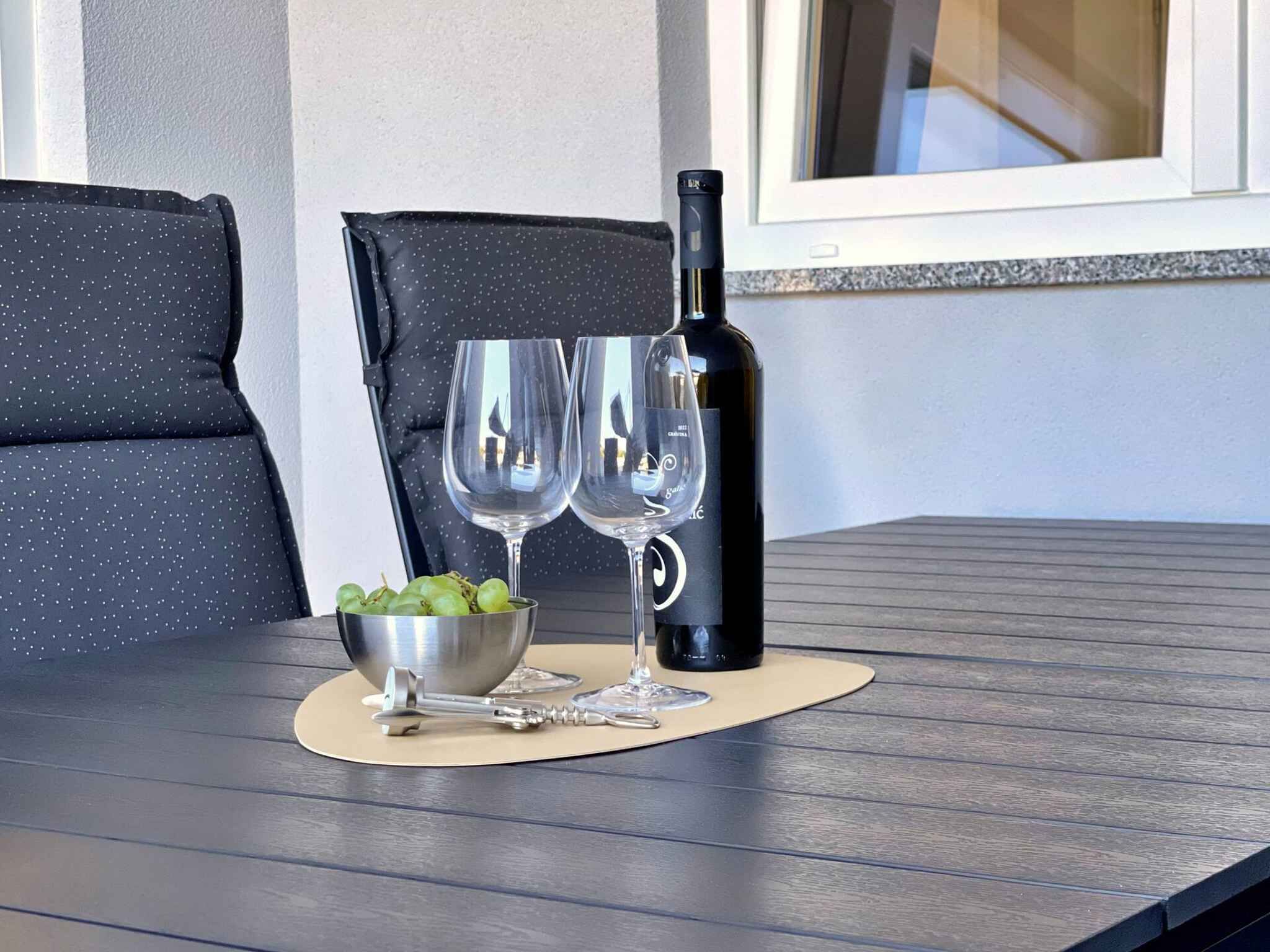 Et bord med en vinflaske, to vinglas, en skål med druer og en korkskrue på et træbord.