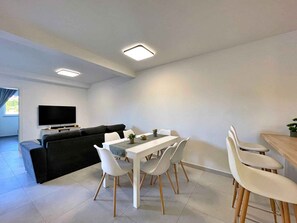 Un salon moderne comprenant un canapé, une table à manger, des chaises et un téléviseur à écran plat.
