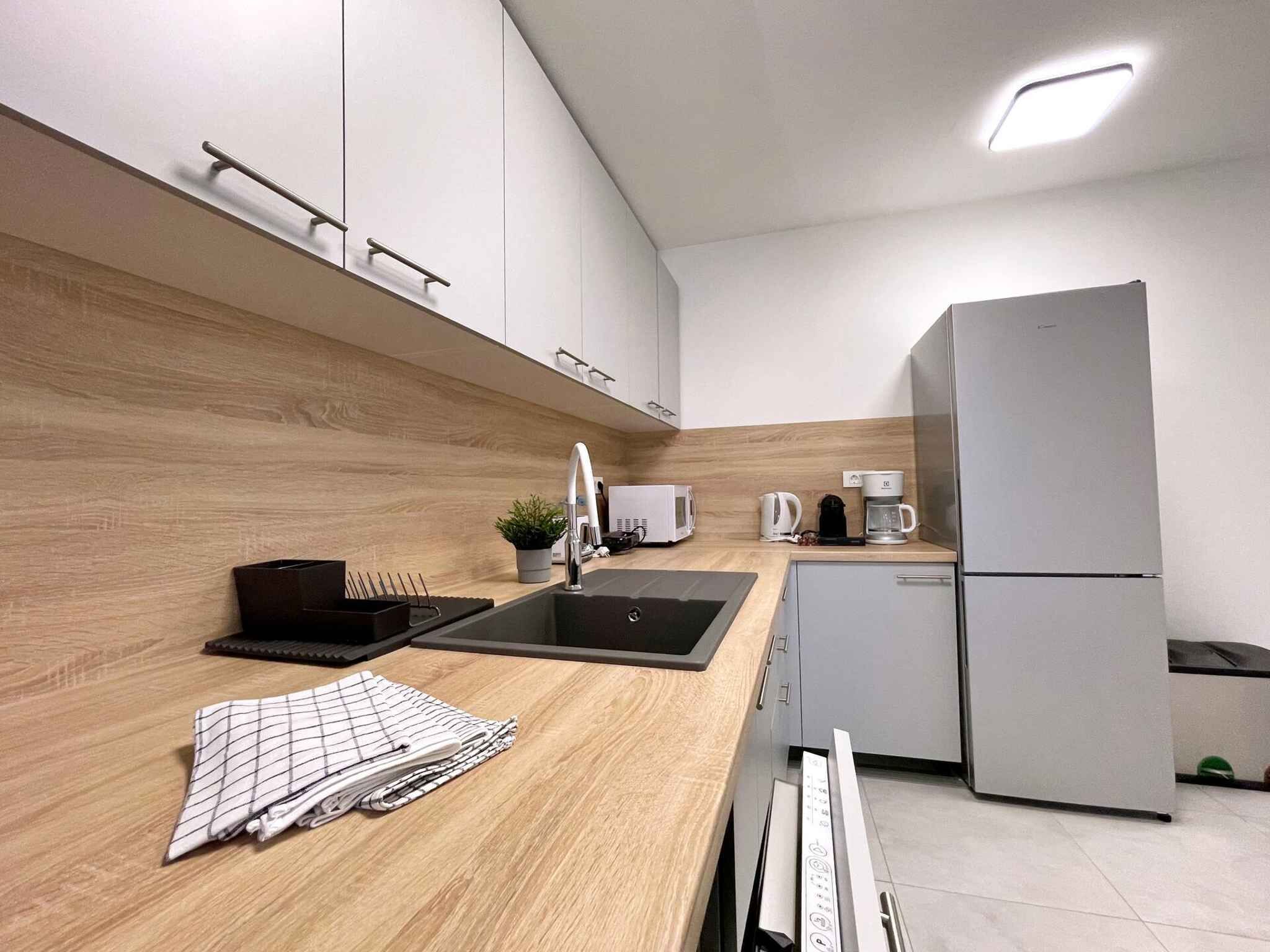 A modern kitchen with a wooden countertop, a sink, a coffee maker, and a refrigerator.