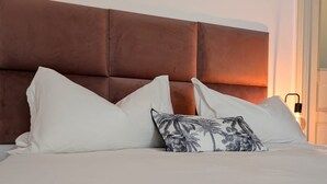 A bed with a brown upholstered headboard, white pillows, and a single decorative pillow with a palm tree pattern. - Very large apartment in center the only one in Sicily with private cinema room. (Catania)