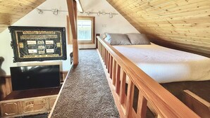 A bedroom with a sloped ceiling, wooden walls, a bed, a TV, and a framed picture on the wall.