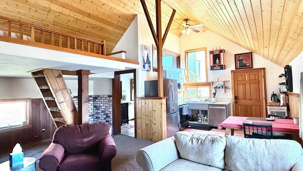 A spacious loft with a high ceiling, a staircase, a kitchen area, and a living room with a sofa and armchair.