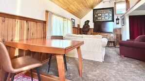 A cozy room with a wooden ceiling, a dining table, a sofa, and a television.
