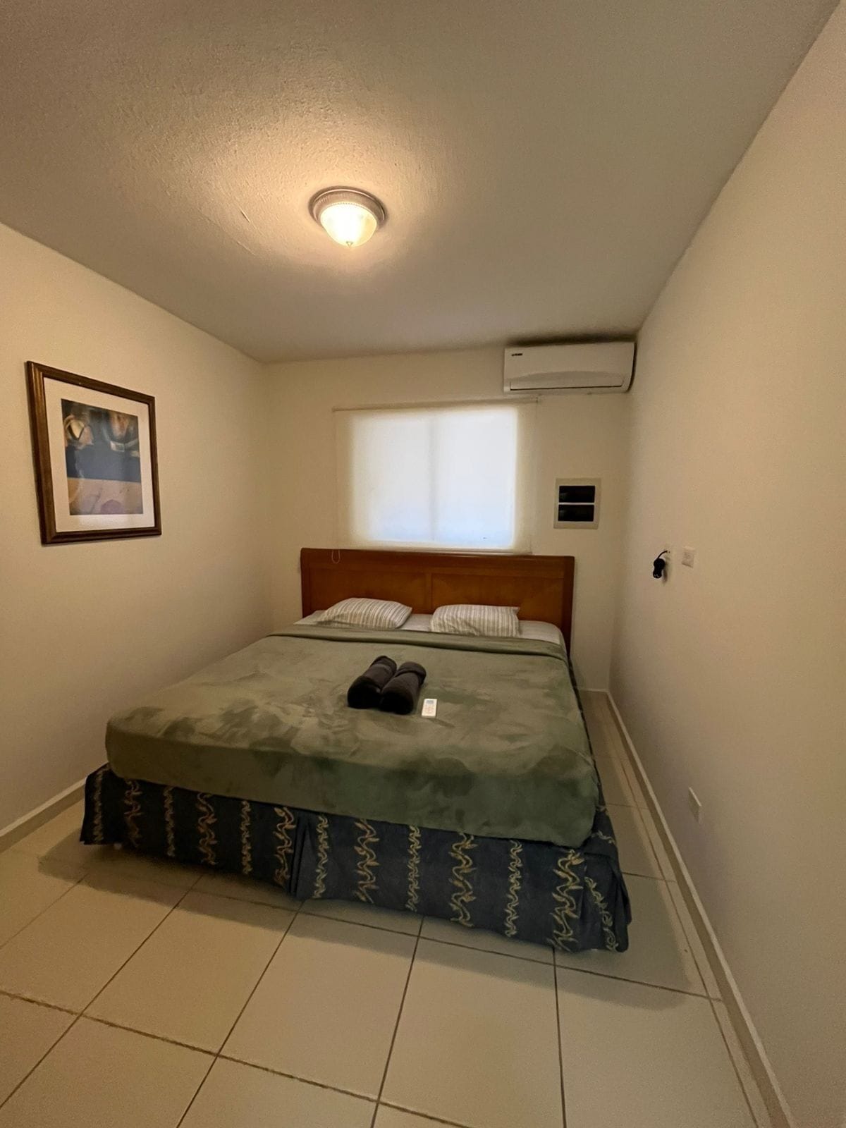 Un dormitorio pequeño y ordenado con una cama individual, un cuadro en la pared y un ventanal que proporciona luz natural.