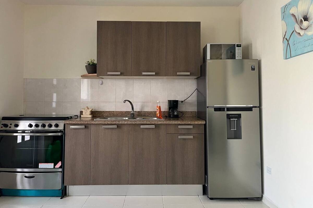 Una cocina moderna con armarios de madera, un refrigerador de acero inoxidable, horno empotrado y cafetera.