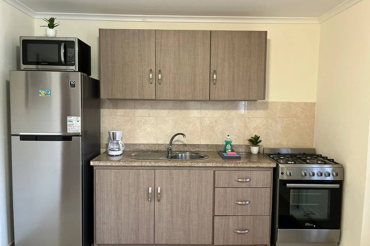 Una cocina compacta con refrigerador, microondas, cafetera, lavaplatos y estufa.