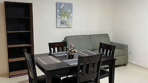 Un comedor con una mesa dispuesta para cuatro personas, rodeada de sillas, una estantería y un cuadro en la pared.