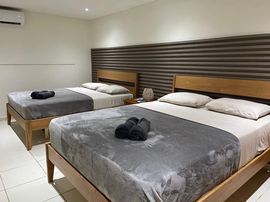 A hotel room with two beds, each with grey bedding and wooden headboards. There is a small table with a lamp between the beds.