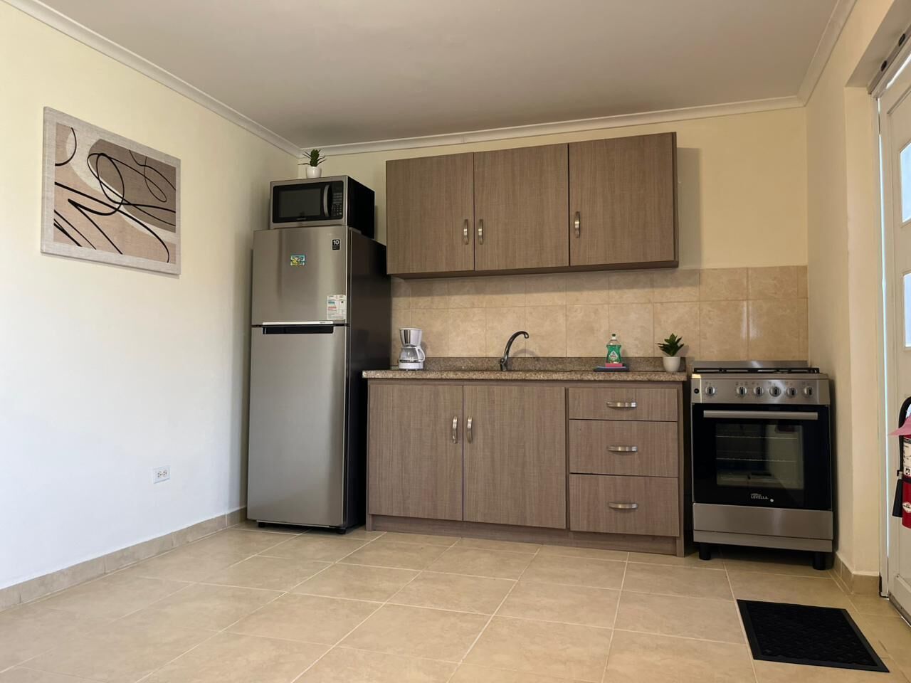 Una cocina equipada con refrigerador, microondas, cafetera, horno y alacenas.
