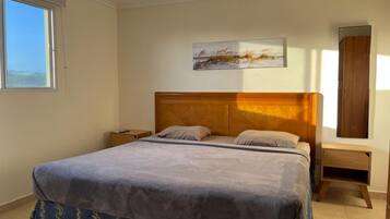 Un dormitorio con cama, mesita de noche, cabecera de madera, un cuadro en la pared y ventana.