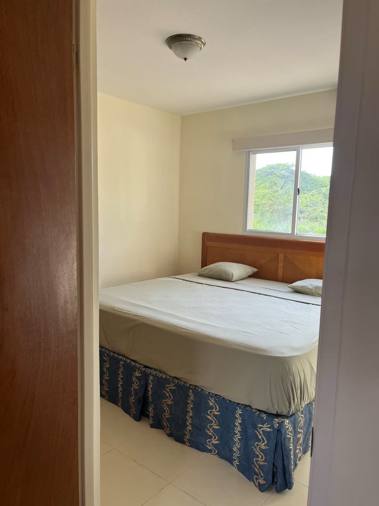 Un dormitorio con una cama individual, una ventana con vista a la vegetación y una lámpara en el techo.