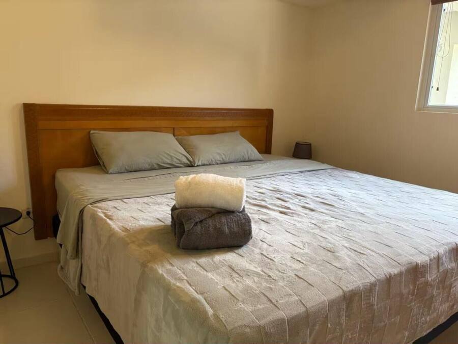 Una cama bien hecha con cabecera de madera, una mesita de noche y una ventana con cortinas.