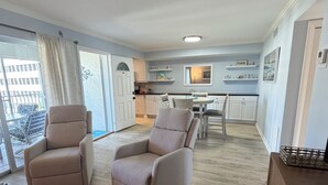 A modern living room with two beige armchairs, a dining table, and a kitchen in the background.