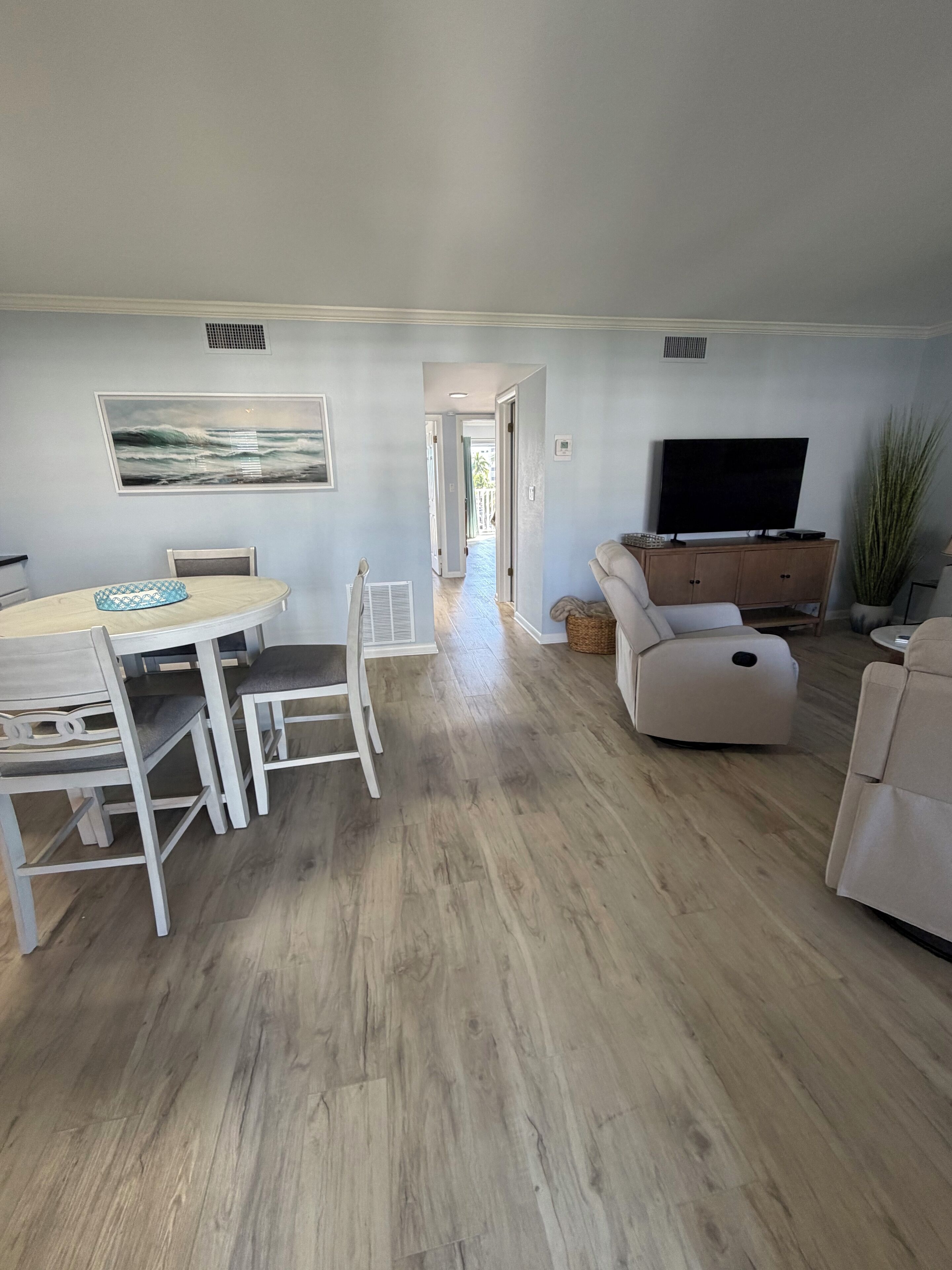A spacious living area with a dining table, chairs, a sofa, a TV, and a plant.