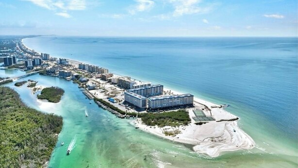 An aerial view of a coastal hotel with multiple buildings, a marina, and clear blue waters.