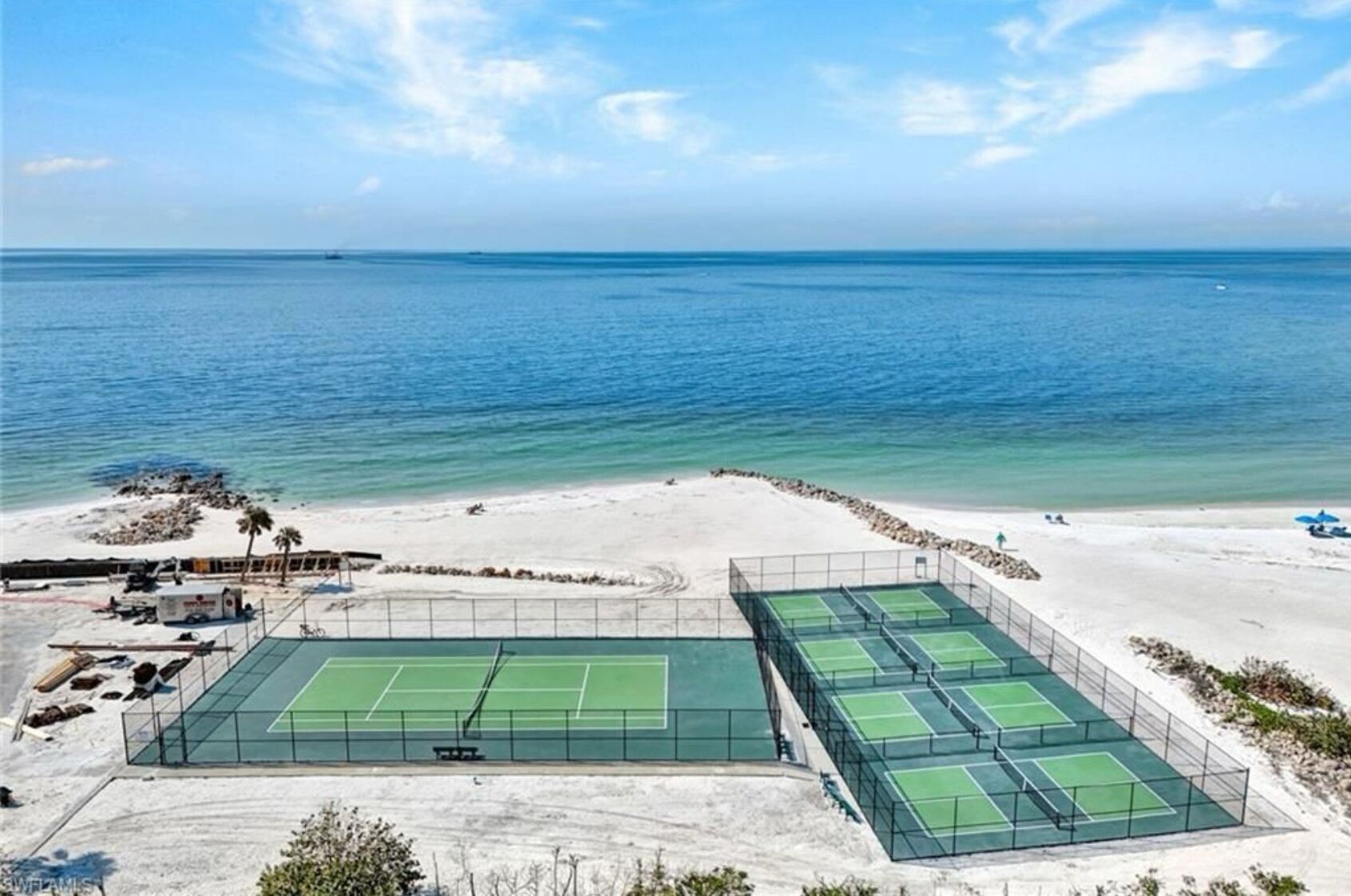 Ein Tennisplatzkomplex mit mehreren Plätzen, einem Sandstrand und Blick aufs Meer.