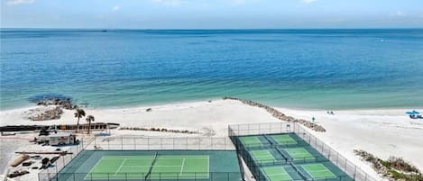 Un complejo de canchas de tenis con varias canchas, una playa de arena y vista al océano.