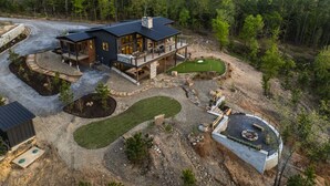 A modern two-story house with a large deck, a landscaped yard with a putting green, and a stone fire pit.