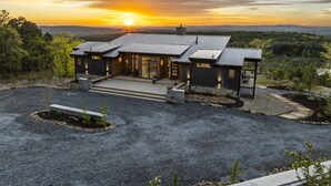 A modern house with a large deck, surrounded by a gravel driveway and landscaped areas.