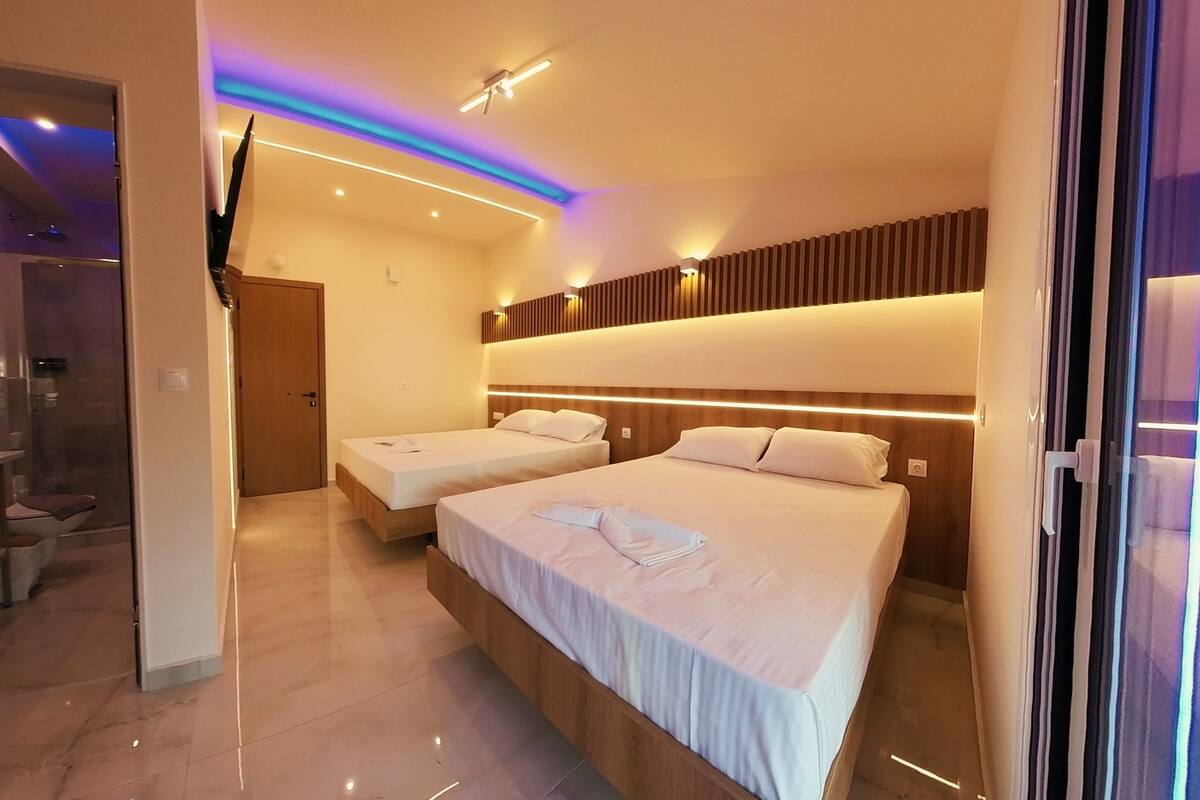 Une chambre d’hôtel moderne avec deux lits, une salle de bain dotée d’une douche en verre et un couloir menant à une autre chambre.