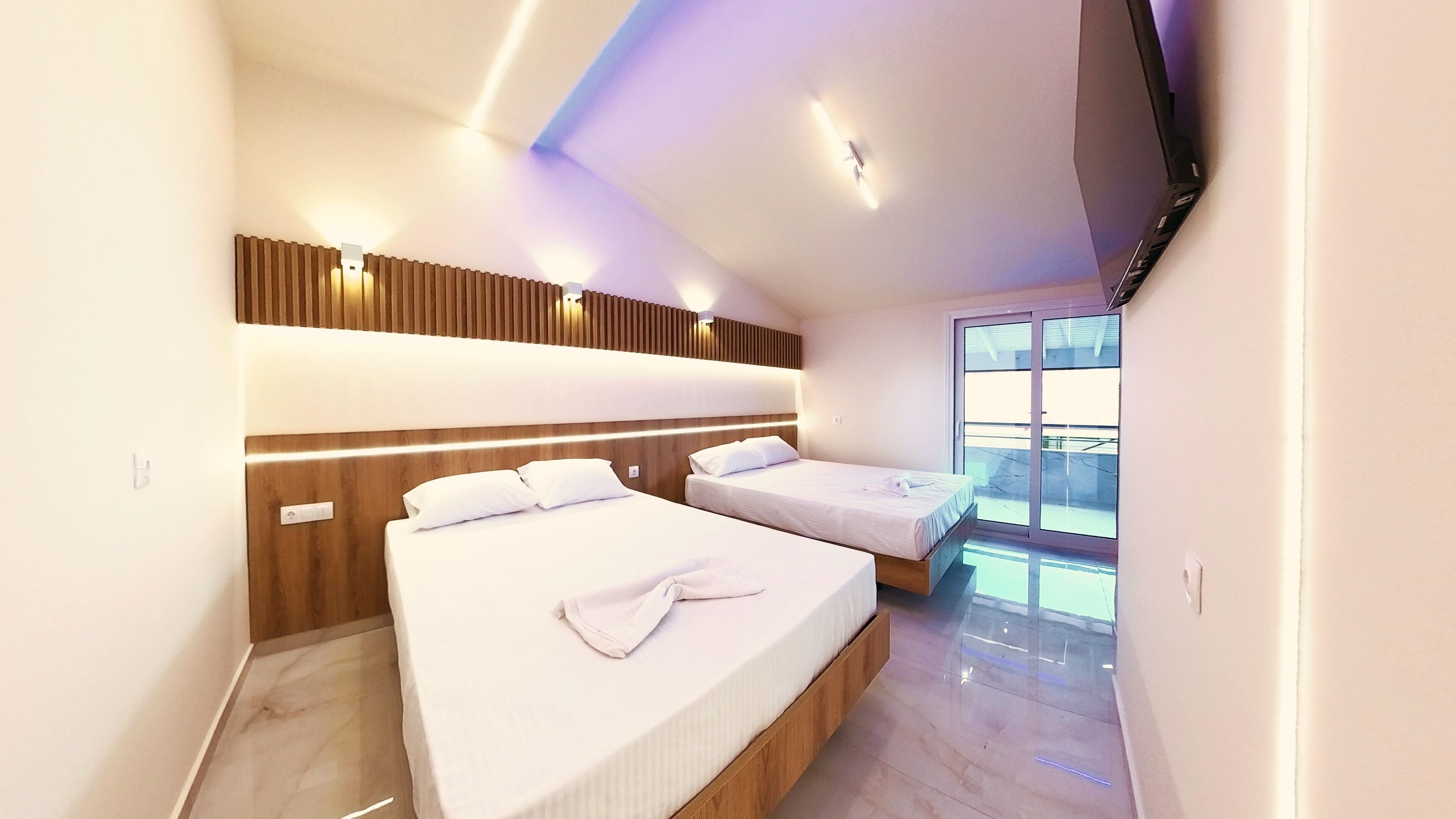 Ein modernes Hotelzimmer mit zwei Betten, einem Holz-Kopfteil, einem großen Fenster und einem Flachbildfernseher.