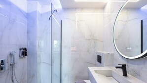 Une salle de bain moderne avec une douche à l’italienne en verre, un mur recouvert de carreaux de marbre, un miroir rond et un robinet noir.
