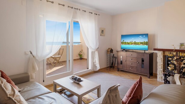 A living room with a sofa, a coffee table, a TV, and a view of the sea through a glass door. - Casa Feliz Penthouse by Mabiente (Mijas)