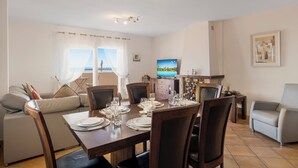 A dining area with a table set for four, a sofa, and a television on the wall. - Casa Feliz Penthouse by Mabiente (Mijas)