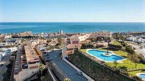 A coastal cityscape with a prominent swimming pool surrounded by greenery and a view of the sea. - Casa Feliz Penthouse by Mabiente (Mijas)