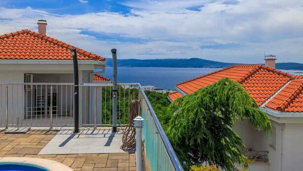 A residential area with red-tiled roofs, a swimming pool, and a view of the sea.