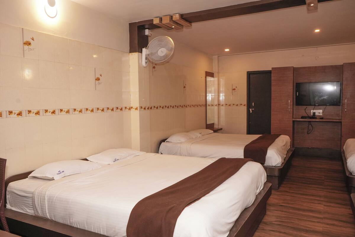 A hotel room with two beds, a TV, a fan, and a wooden floor.