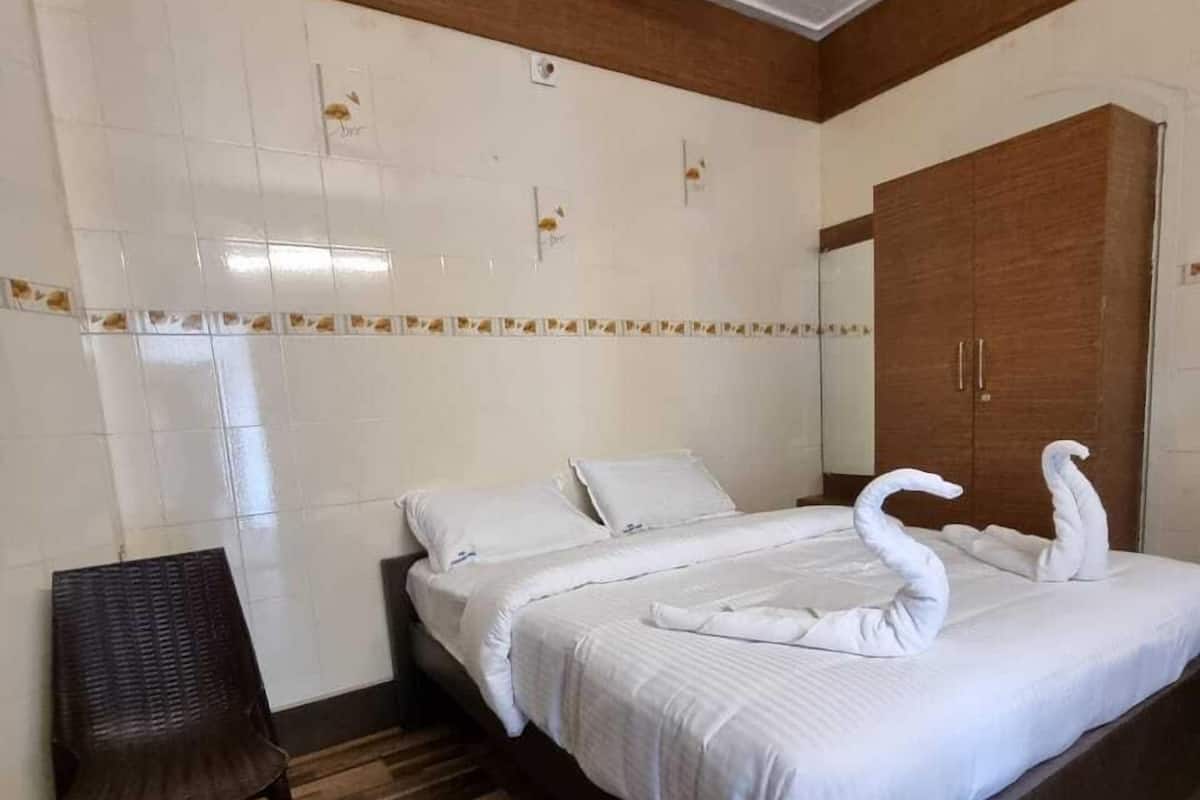 A hotel room with a bed, a wooden headboard, a brown chair, a wooden floor, and a wardrobe.