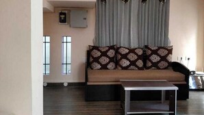 A living room with a sofa, a coffee table, and a wall-mounted clock. - Hk Grand Inn By K Hotels (Yercaud)
