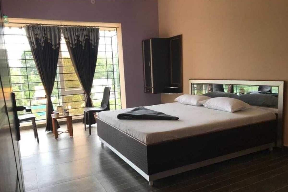 A modern bedroom with a large bed, a TV mounted on the wall, and a window with curtains.