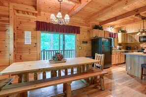 A wooden cabin with a dining table, benches, a refrigerator, and a kitchen area. - Tall Timbers Lodge | Hocking Hills, 5BR, Pets (Logan)