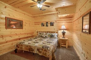 A wooden cabin bedroom with a bed, a ceiling fan, a framed picture, and a lamp on a nightstand. - Tall Timbers Lodge | Hocking Hills, 5BR, Pets (Logan)
