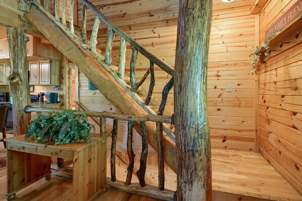 A wooden interior with a rustic staircase, a wooden desk with a plant, and a wall with a sign.