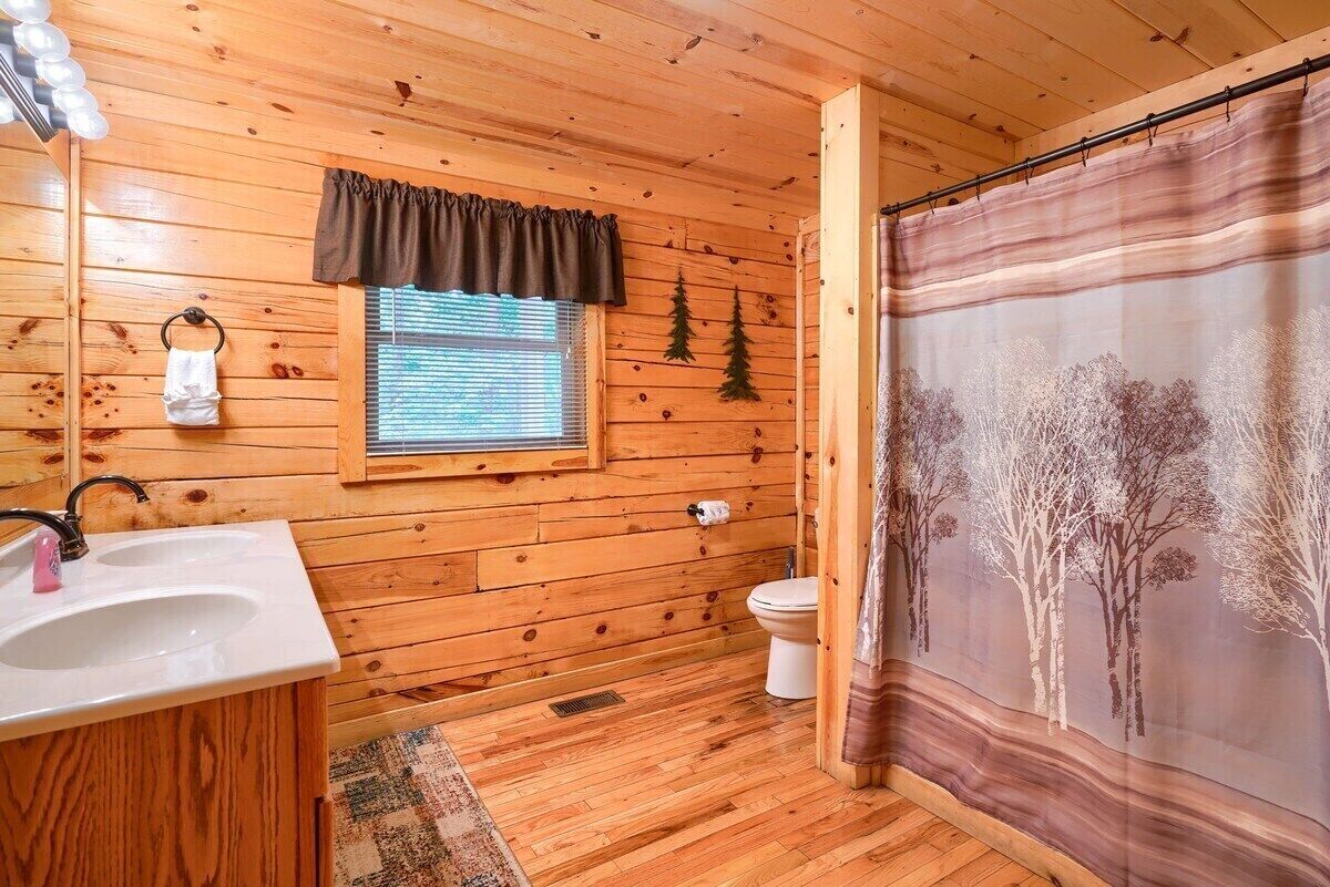 A wooden cabin bathroom with a sink, toilet, and shower curtain.
