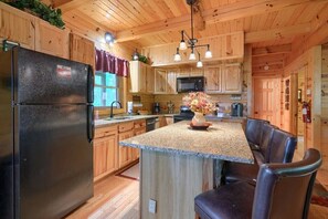 A wooden cabin kitchen with a granite countertop island, a refrigerator, and a microwave.